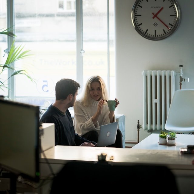 Business Discussion and Team Collaboration Two professionals having a discussion over a laptop in a casual office setting, representing teamwork and collaboration