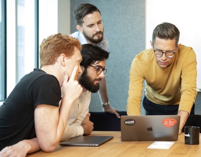 Group of professionals collaborating around a laptop, discussing business strategy and analyzing data in a modern office environment