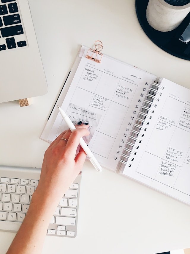 Work Planning and Task Scheduling on Desk Person writing in a planner notebook beside a laptop and keyboard, organizing daily tasks and work schedule